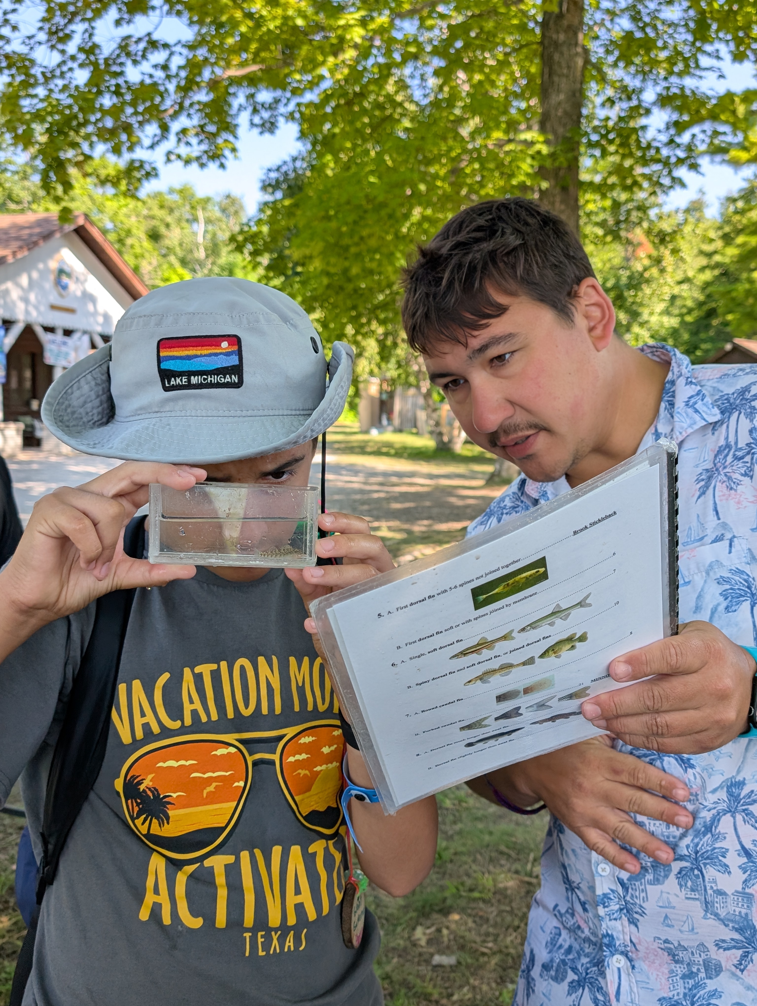 two people look at a small fish in a container and try to identify it