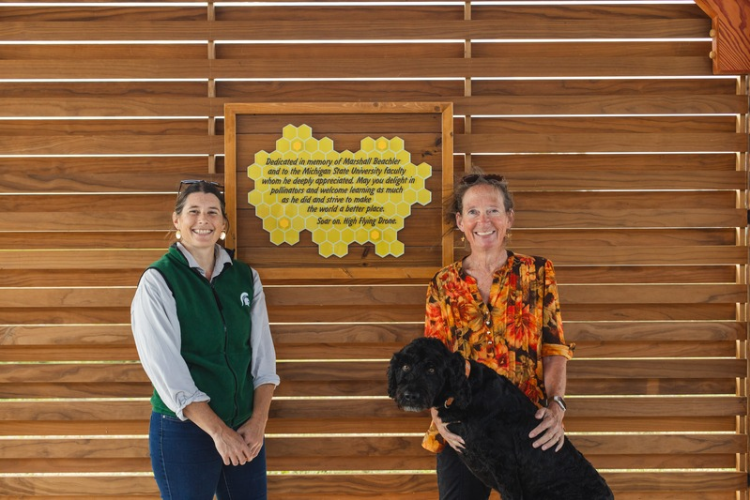 Dr. Meghan Milbrath, Charlotte Hubbard and Hubbard's dog Clover pictured in front of the new plaque at the MSU Pollinator Performance Center Teaching Pavilion honoring the legacy of Marshall Beachler.