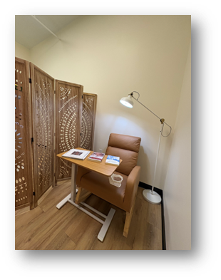 A cozy breastfeeding nook with a leather chair, small table with books and a mug, and a decorative wooden room divider.