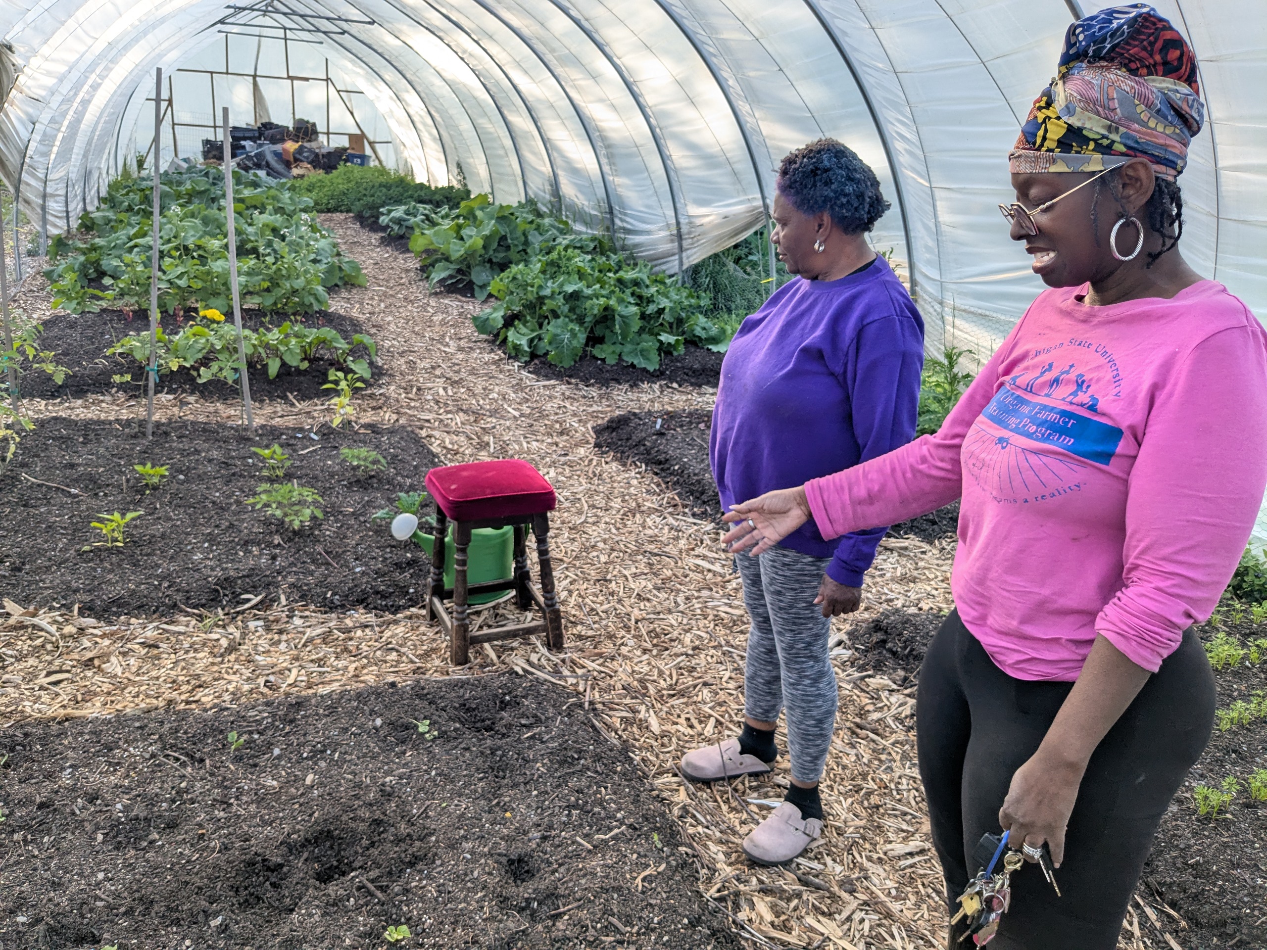Two women in a hoophouse with vegetable plantings.